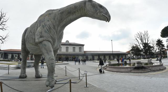 Sconvolgente ritrovamento in una piazza: un uomo morto dentro alla zampa di un dinosauro di cartapesta